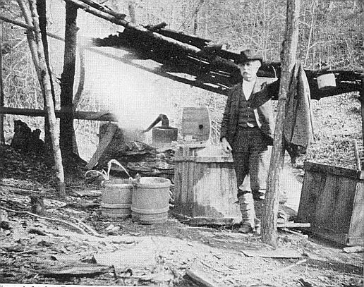 MOONSHINING. Revenue officers hot on the trail; the fire
is burning, the still working, and the moonshiner's coat hangs on a
tree. (Brown Bros.)