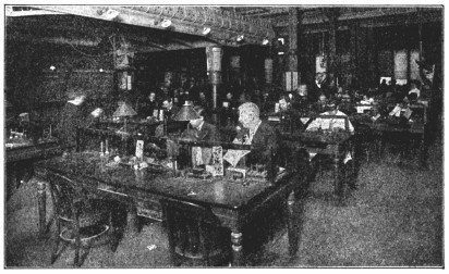 A photograph of a large office filled with men sitting at tables.
