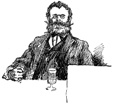 A bearded man wearing glasses sits with a glass before him.