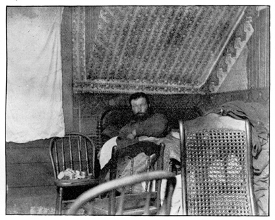 A bearded man lies in a small bed.