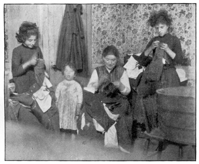 A woman and two young girls sew, while a toddler looks at the camera.
