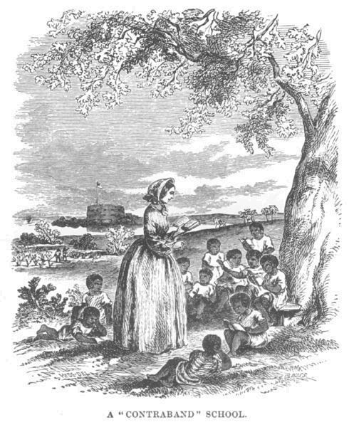 A group of children sit under a tree, a teacher standing in front
of them. A fort can be seen in the background.