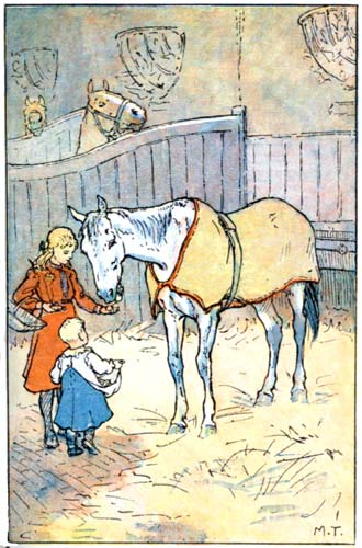 A blanketed horse in his stall, being fed treats by two children