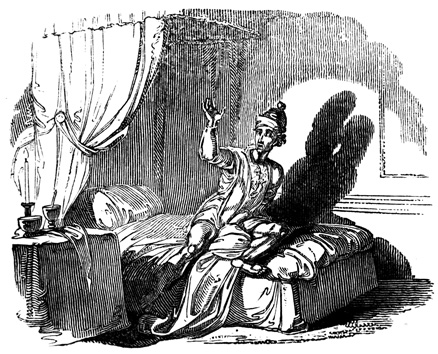 A man sits on his bed, hand in the air.