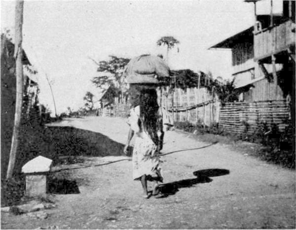 NATIVE GIRL CARRYING BASKET OF CLOTHES.