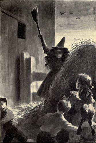 'Witch' jumping out from behind a haystack toward group of young people seated on the ground