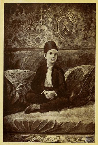 Boy wearing a fez sitting amongst pillows on the floor with legs crossed