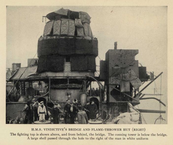 H.M.S. VINDICTIVE'S BRIDGE AND FLAME-THROWER HUT (RIGHT). The fighting top is shown above, and from behind, the bridge. The conning tower is below the bridge. A large shell passed through the hole to the right of the man in white uniform.