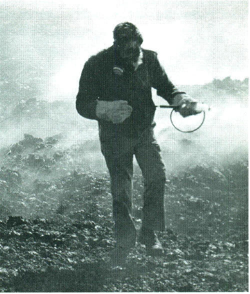 Scientist, wearing asbestos gloves and gas mask, samples volcanic gases from active vent.