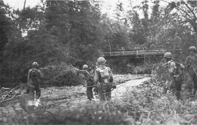 A PATROL OF THE 307TH INFANTRY warily approaches a river crossing near Camp Downes.