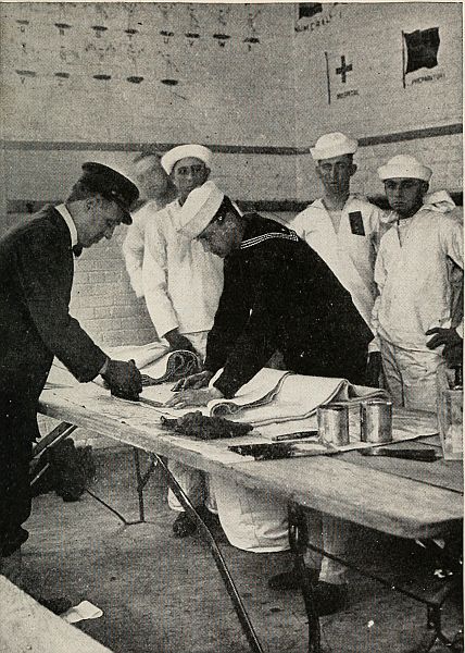 Man folding cloth on table while other sailors watch