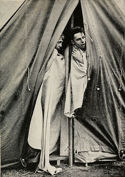 two men in blankets peering out of a tent flap