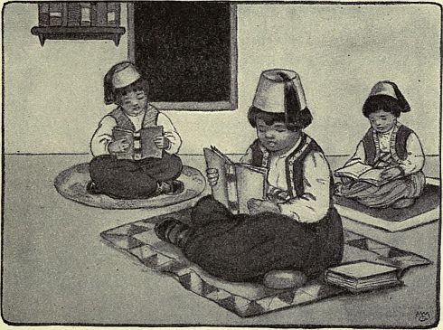 three boys, wearing fezes, sitting on mats reading