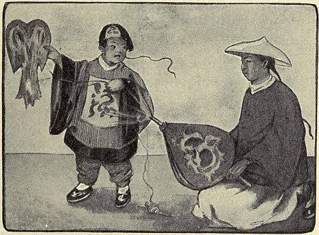 Child holding up kite, man on ground holding bellows