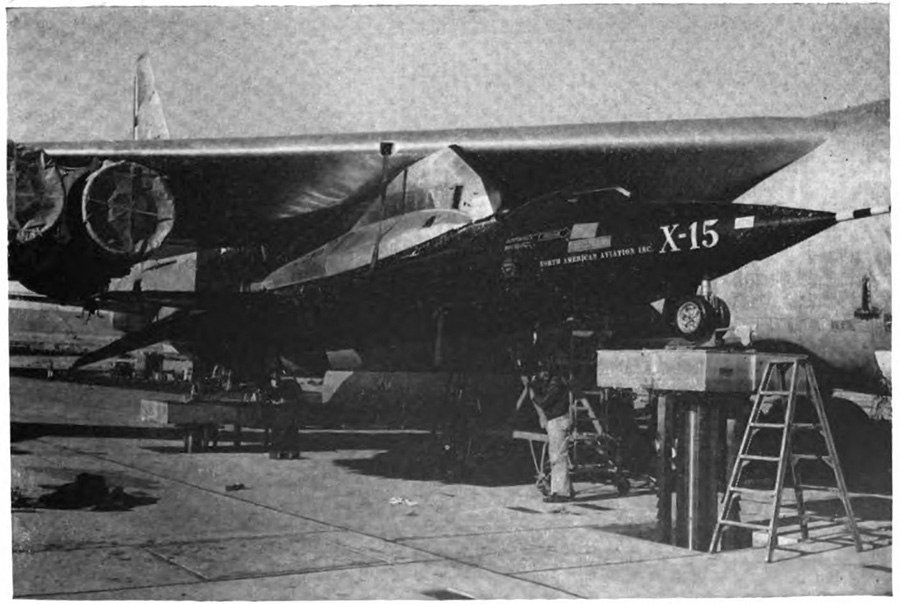 A small plane attached to the underside of a larger one with ladders around it