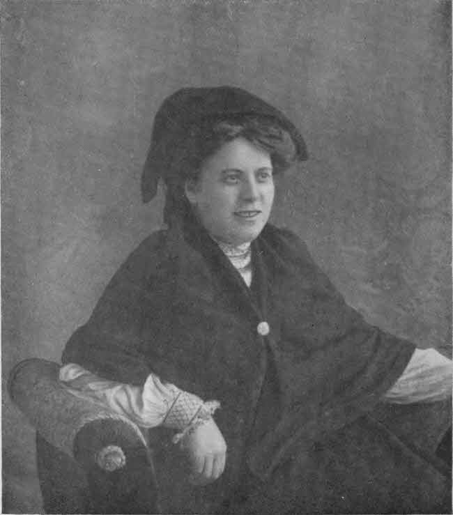 The upper body of the author is shown formally posed seated, with a soft hat-like covering for much of her hair and a shawl with a clasp over a long-sleeved blouse.