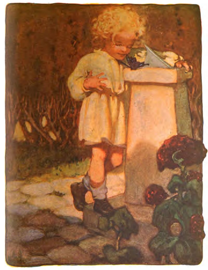 A young child with blonde curly hair stands on a stone path, surrounded by flowers and shrubs. The child wears a light tunic or smock dress, dark shoes, and rolled socks. They look closely at a dark butterfly resting on a stone pedestal with a sundial.