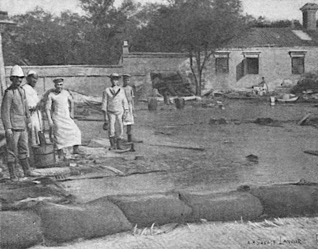Liquid on ground, with some men on solid ground to the left and a building in the background