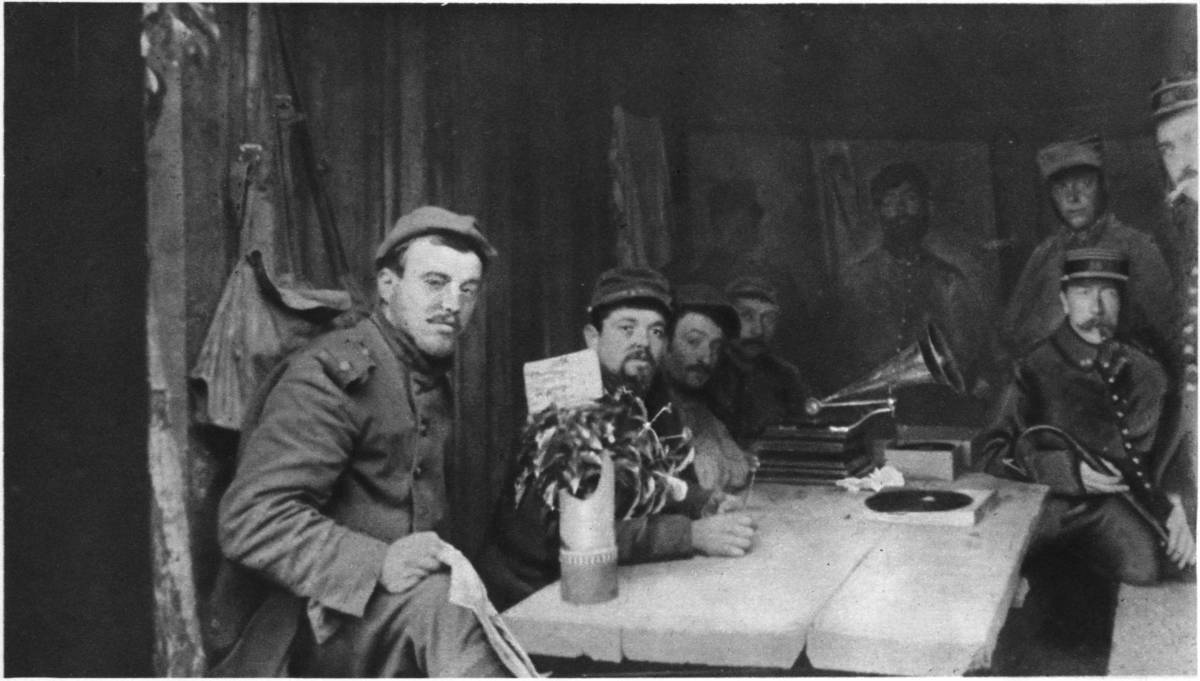 UNDERGROUND, WITH GRAMOPHONE, WHITE TABLE-COVER, AND FLOWERS: FRENCH SOLDIERS IN A "HOME-LIKE" BOMB-PROOF TRENCH.