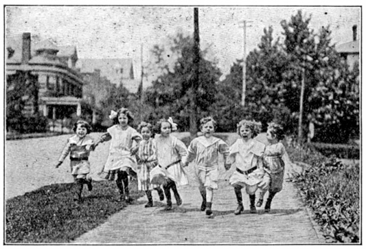 A photograph of boys and girls holding hands and running down the sidewalk