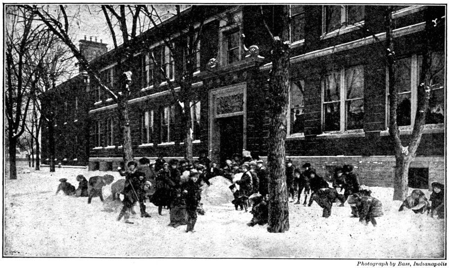 A photograph of children playing in the snow outside of school.