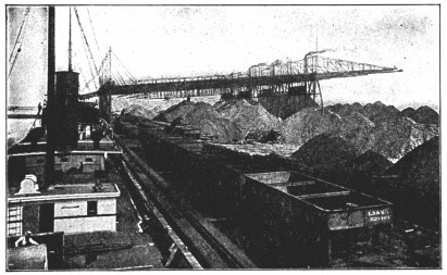 A photograph of huge piles of ore next to rail cars.