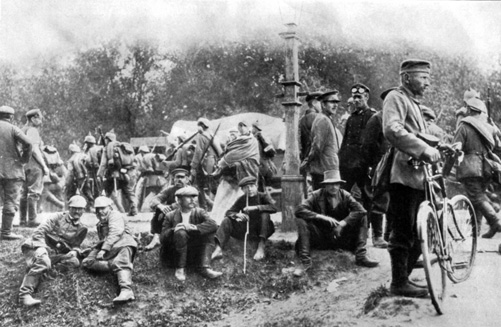 Feldgraue auf dem Marsch. Vorn plaudernde deutsche Soldaten und polnische Dorfbewohner.