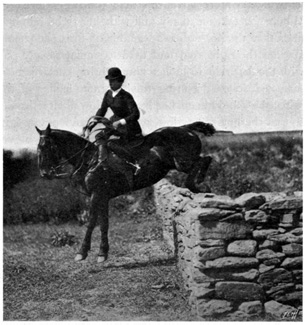 Horse jumping a stone wall with a woman riding side-saddle
