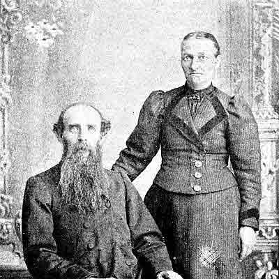 Husband: long grizzled beard. Wife: high-neck dark blouse, brooch at throat.