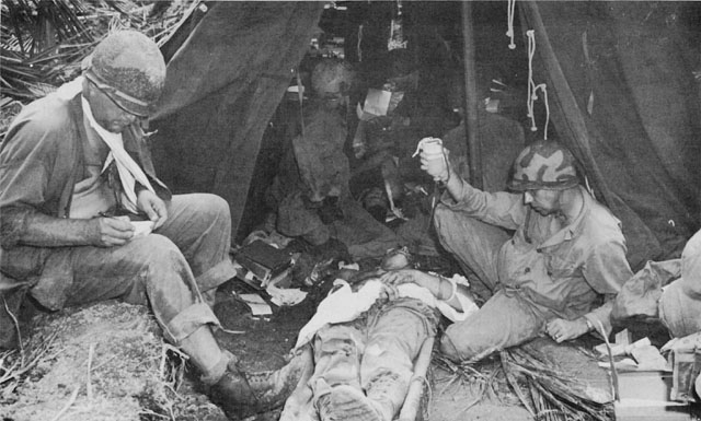 A CASUALTY RECEIVES TREATMENT at a forward aid station.