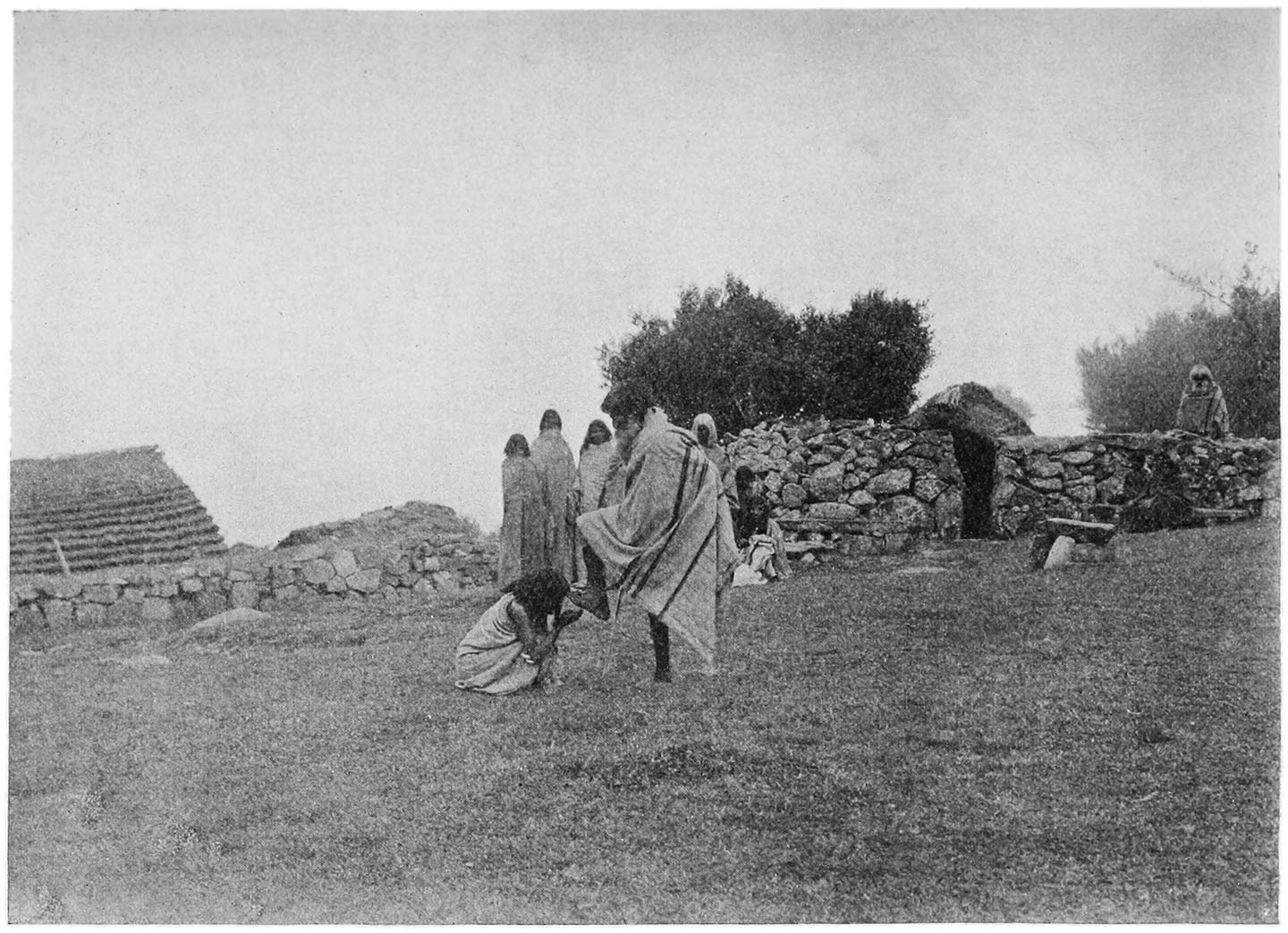 FIG. 12.—THE ‘KALMELPUDITHTI’ SALUTATION TAKING PLACE AT THE VILLAGE OF NÒDRS. ON THE LEFT IS THE HOUSE; ON THE RIGHT IS THE LESS IMPORTANT DAIRY OF THE VILLAGE (THE ‘TARVALI’), AND IN FRONT OF IT IS THE STONE CALLED ‘MENKARS.’