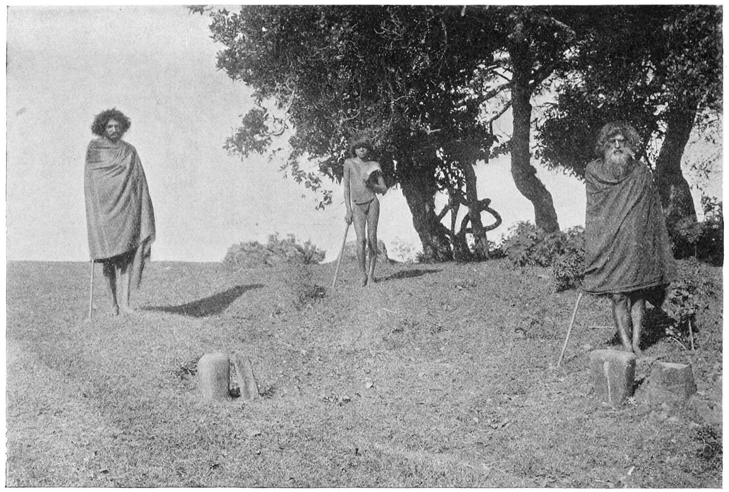 FIG. 33.—THE FOUR ‘NEURZÜLNKARS’ AT MÒDR. BEHIND THE STONES ON THE RIGHT IS KARKIEVAN, THE ‘PALOL’ OF THE ‘TIIR’; ON THE LEFT IS NERPONERS, THE ‘PALOL’ OF THE ‘WARSIR’; IN THE CENTRE IS THE ‘KALTMOKH,’ KATSOG, CARRYING A SICKLE-SHAPED KNIFE.