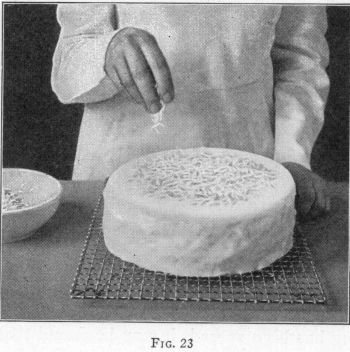 [Illustration: FIG. 23, Sprinkling iced cake with garnish.]